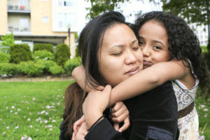 African American Mixed Daughter Kissing Asian Mother on Cheek, Copyspace
