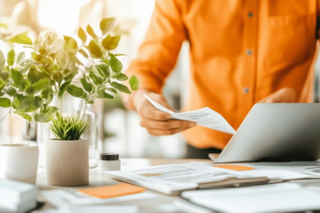 A property management professional reviewing documents beside a laptop, with no visible resident information, EIV Citizenship Verification
