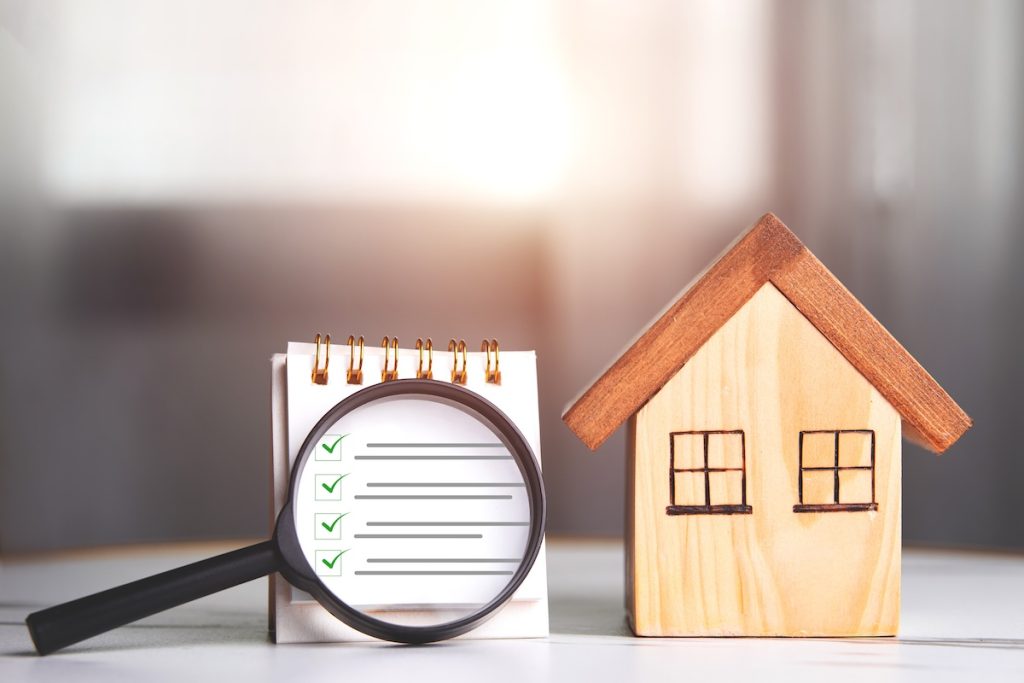 Home inspections, standards according to the requirements, certifications, and real estate safety. Wooden house and magnifying glass with a checklist for home with copy space